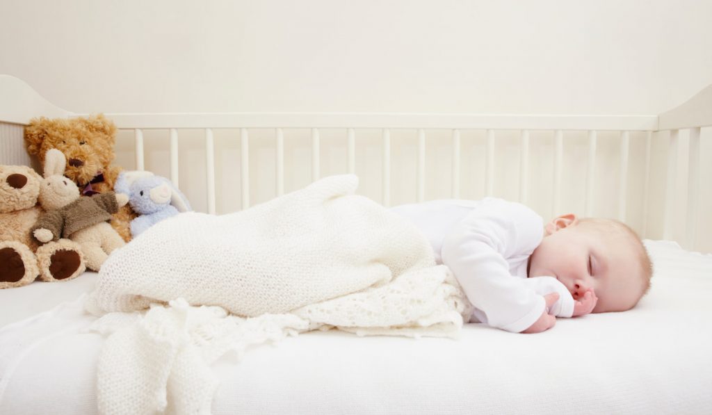 Baby girl sleeping in crib with white blanket