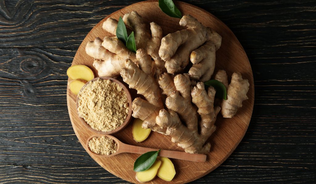 Board with ginger and ginger powder on wooden background
