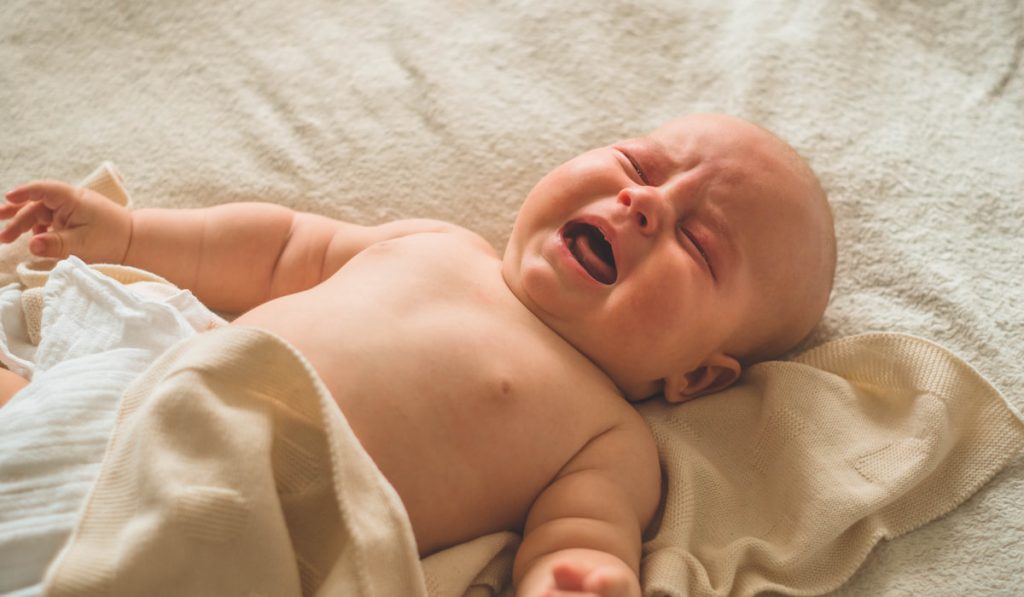Crying tired newborn baby lying on the bed