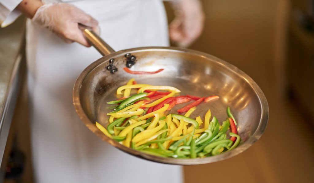 Fragment photo of cook with pan full of cut peppers
