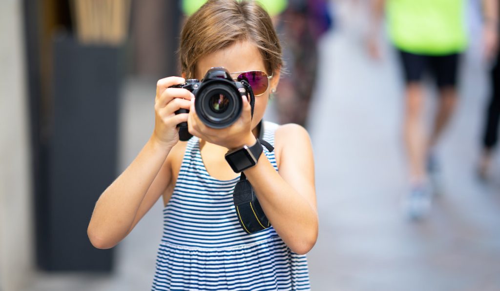 Little girl making photo with DSLR camera on city street
