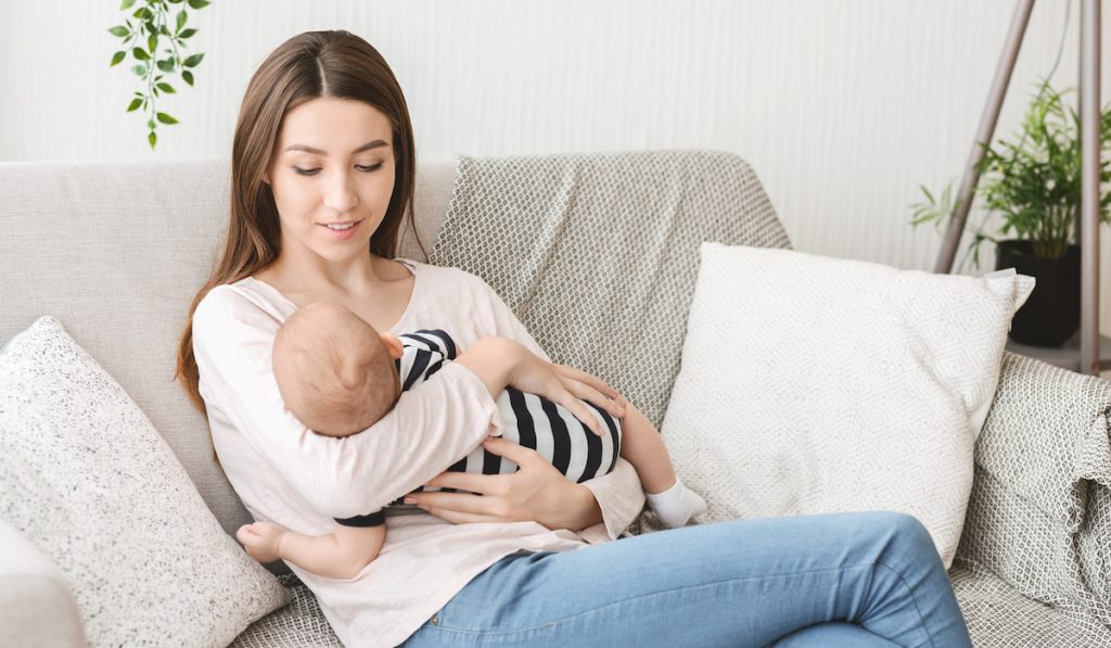 Mom holding newborn child, lulling baby on couch at home
