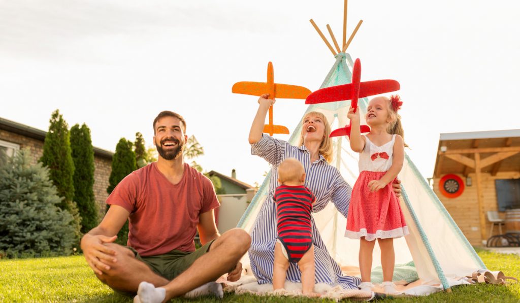 Parents playing with children, throwing toy airplanes while camping in the backyard
