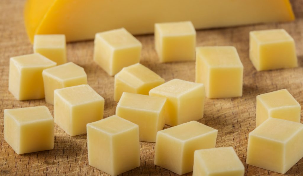 cubes of yellow cheese stacked randomly on wood
