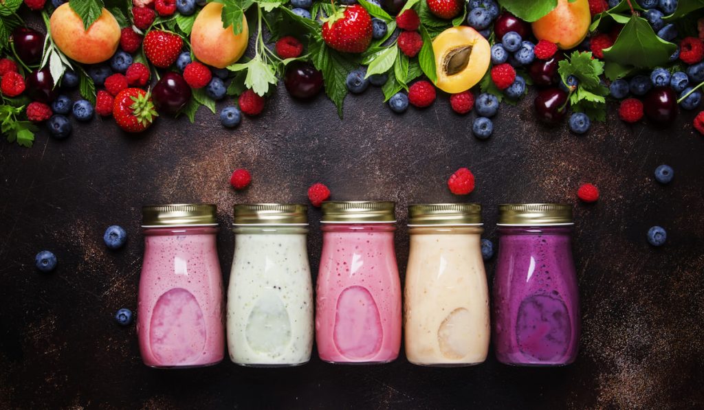 different berry smoothies in a jar and fresh fruits on the background