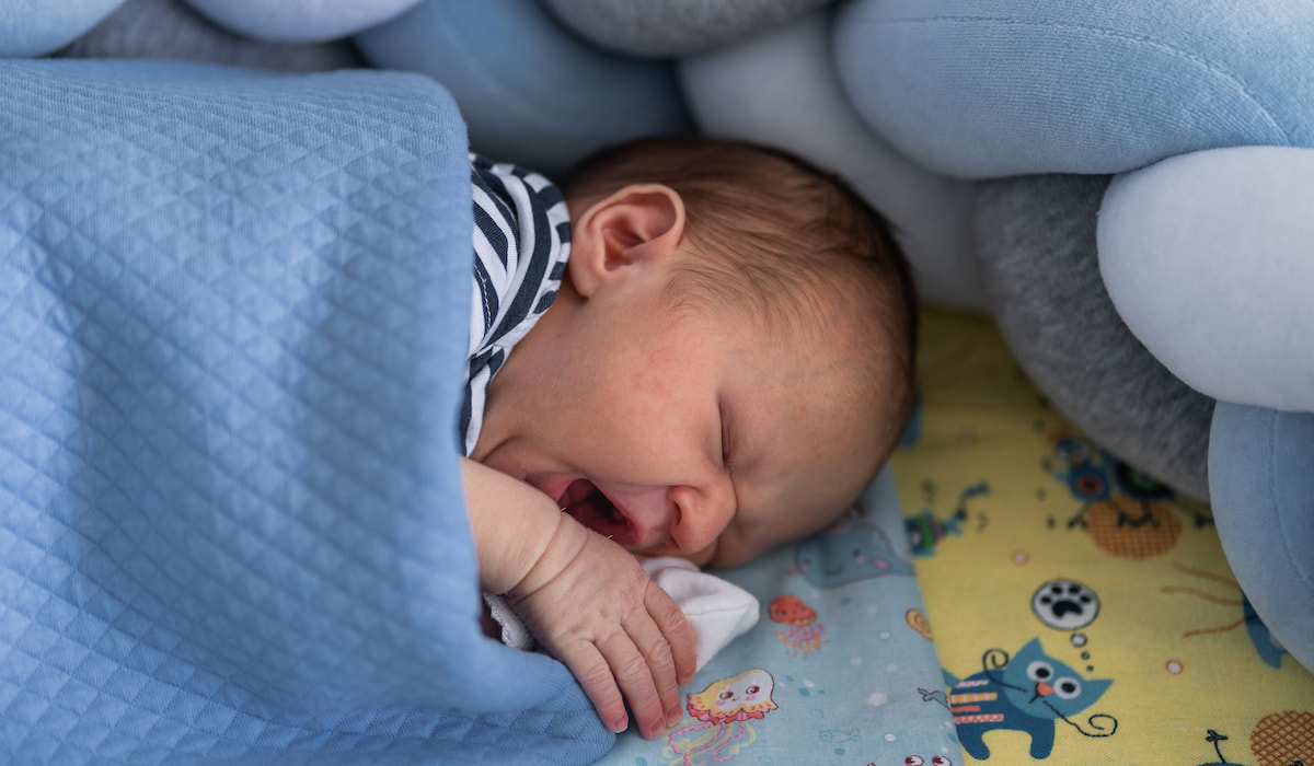 newborn baby yawns while lying in his crib