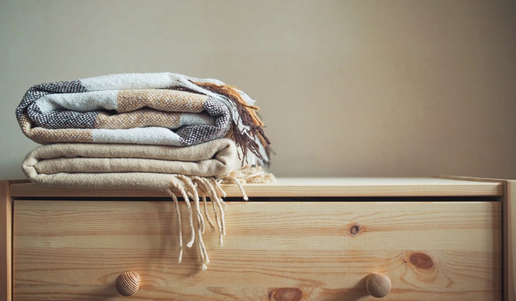 stack of clean beige checkered wool blankets on a wooden chest.